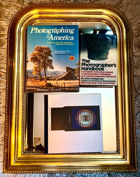 Photographing America by George Hornby and the Editors of Eastman Kodak Company; Color by The Editors of Time-Life Books; The Photographer’s Handbook by John Hedgecoe and a gold-framed mirror.