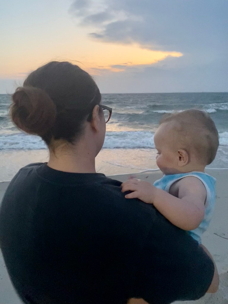 Mother holding her baby by the beach at sunset